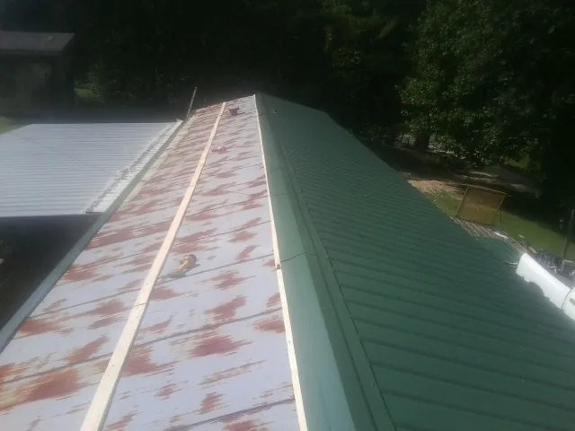 Old rusted panels beside newly installed green metal roofing — Wind Damage Roof Repair by Roofing Brothers in Webster Springs