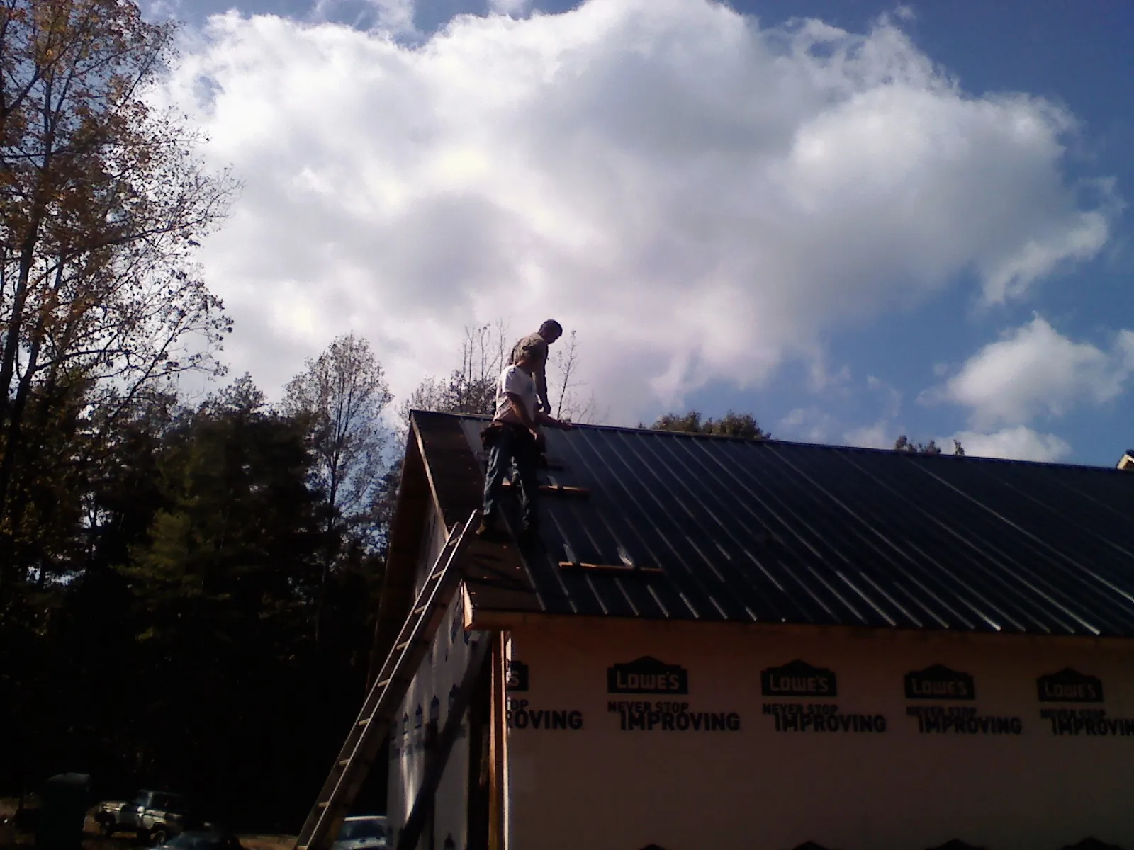 Roofer fastening dark metal panels high against a cloudy sky, from a Roof Inspection job in Webster Springs