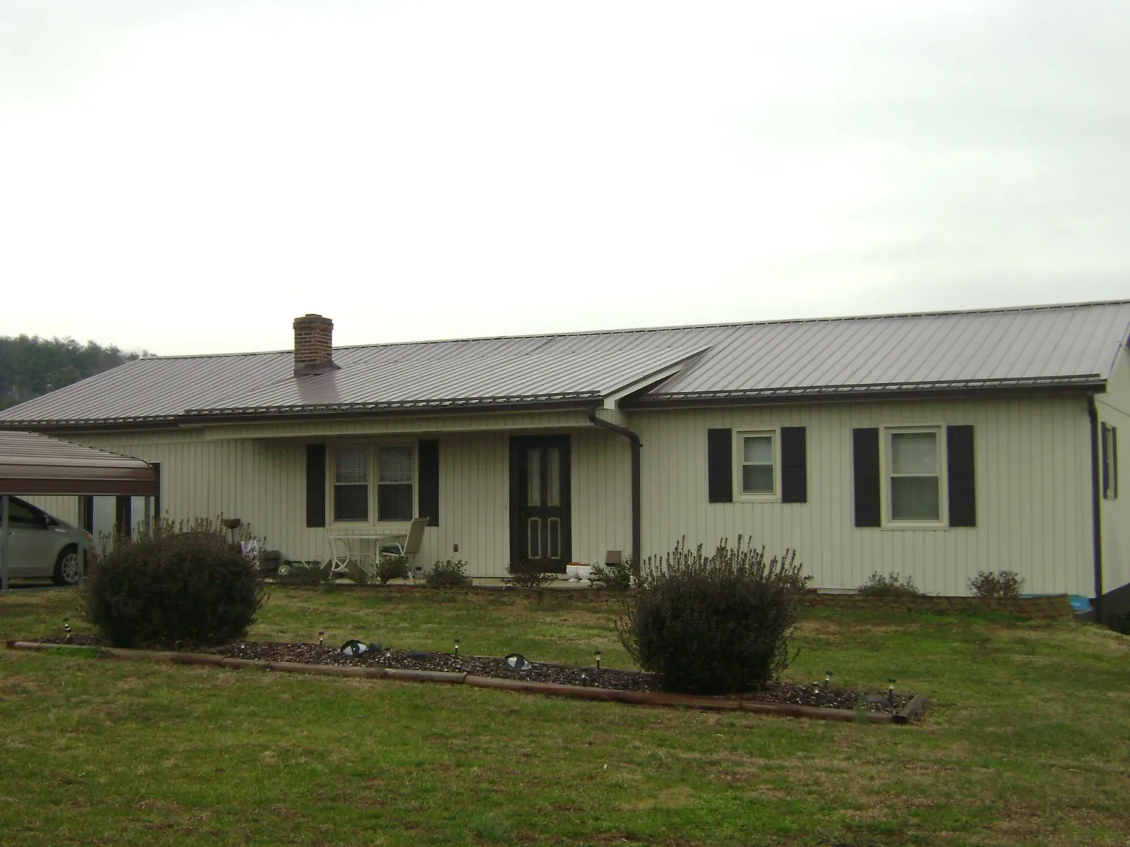 Brown metal roof on a cream sided ranch home with a brick chimney in Webster Springs