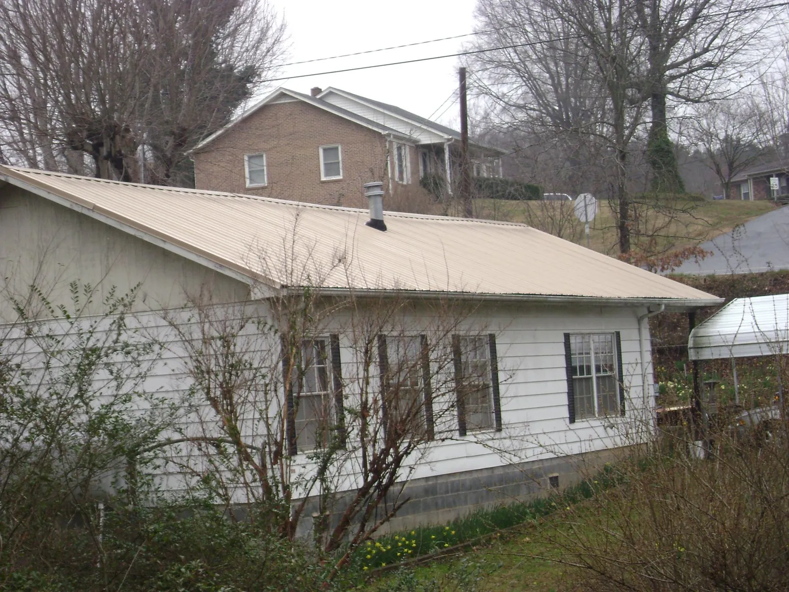 Tan metal roof on a white sided house set into a hillside — Commercial Roofing by Roofing Brothers in Webster Springs