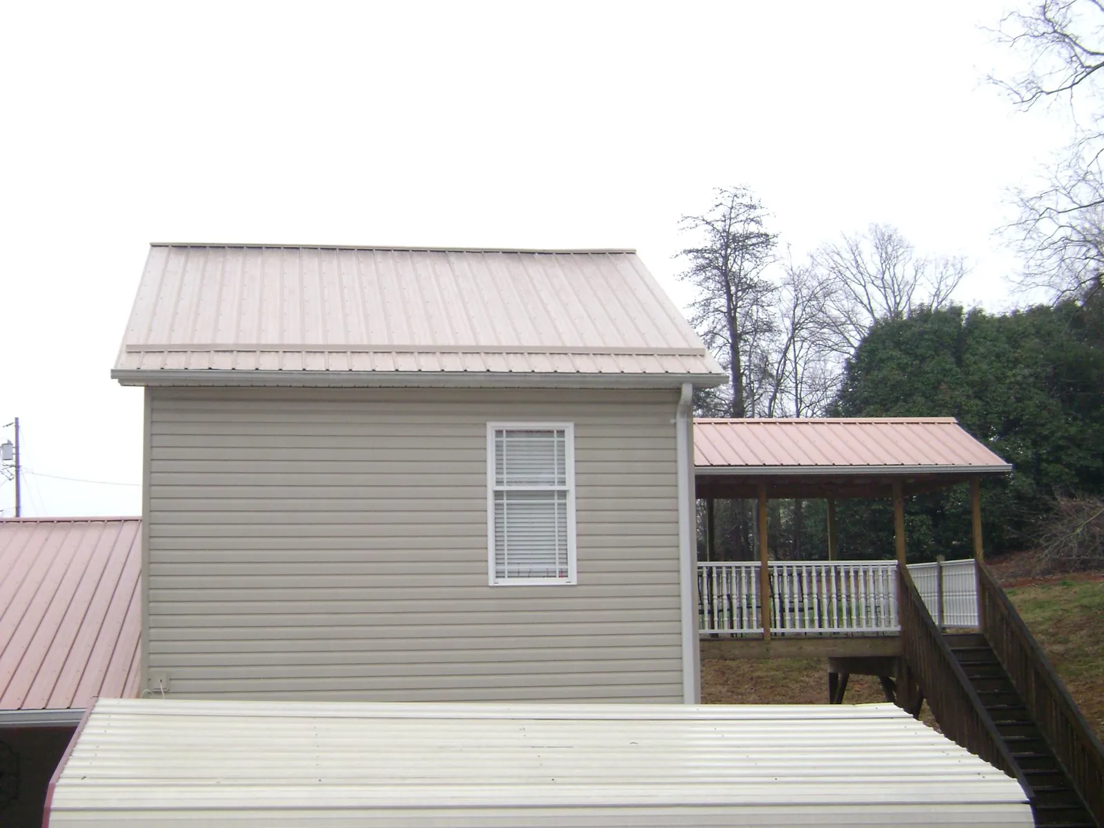 Tan metal roofs on a two story addition and attached porch, from a Roof Replacement job in Webster Springs